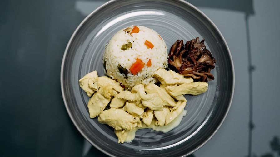 Plato de pollo con arroz, verduras y champiñones servido en cerámica.