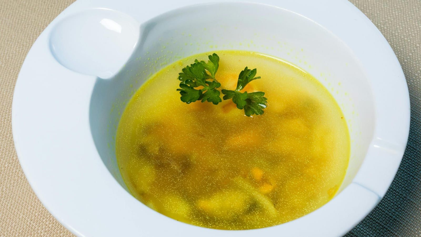 Sopa o caldo de verduras servido en un cuenco blanco.