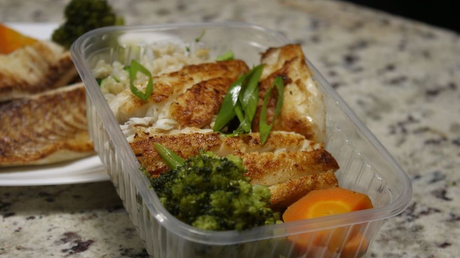 Comida saludable organizada en un recipiente con pollo, brócoli y zanahoria.